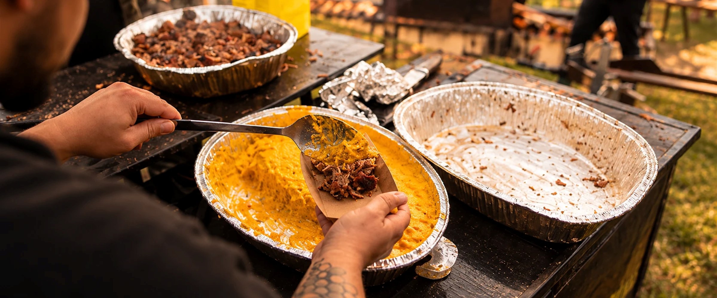 Cozinheiro servindo comida em assadeiras de alumínio em um evento ao ar livre